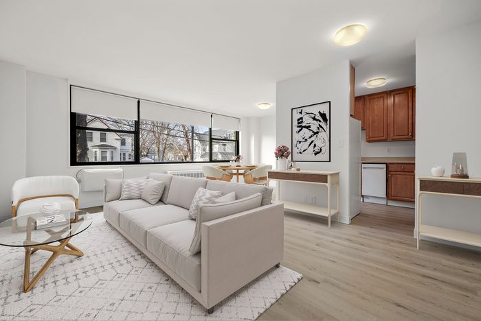 Bright and inviting living room with large windows, modern furnishings, and an open layout leading to a cozy dining area and chic kitchen.