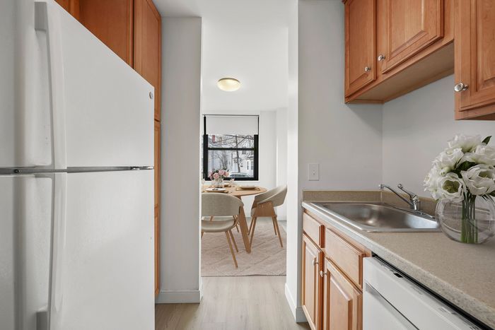 Charming kitchen with wooden cabinets leading to a bright dining area with large window, perfect for cozy meals.