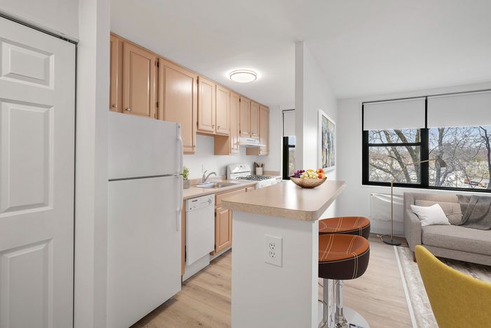 Charming kitchen area with light wood cabinets and modern appliances adjacent to a cozy living room with abundant natural light.