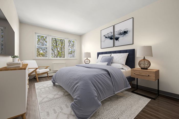 Bright and inviting bedroom featuring a plush bed with soft blue bedding, elegant nightstands, and large windows offering a scenic tree view.