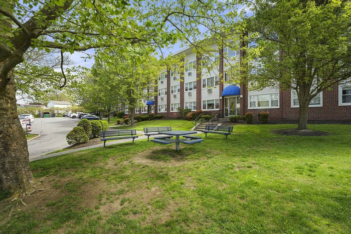 Charming residential building with lush green surroundings, featuring a peaceful sitting area and vibrant trees, perfect for relaxation.