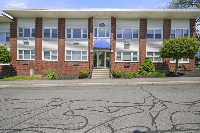 Charming brick apartment building with modern windows and manicured landscaping, showcasing inviting entryway with blue awning.