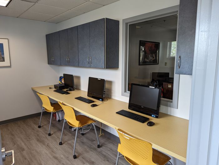 Modern communal workspace featuring sleek computers, vibrant yellow chairs, and ample cabinetry in a bright, inviting setting.