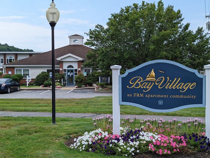 Charming Bay Village apartment community entrance adorned with vibrant flowers and lush greenery, offering a welcoming and picturesque living environment.