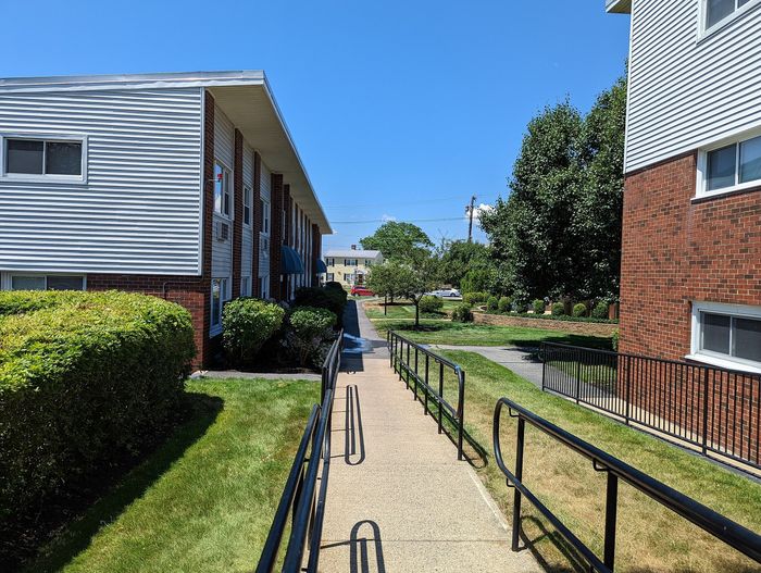 Charming apartment building exterior with well-maintained landscaping and a clear walkway, set against a bright blue sky.