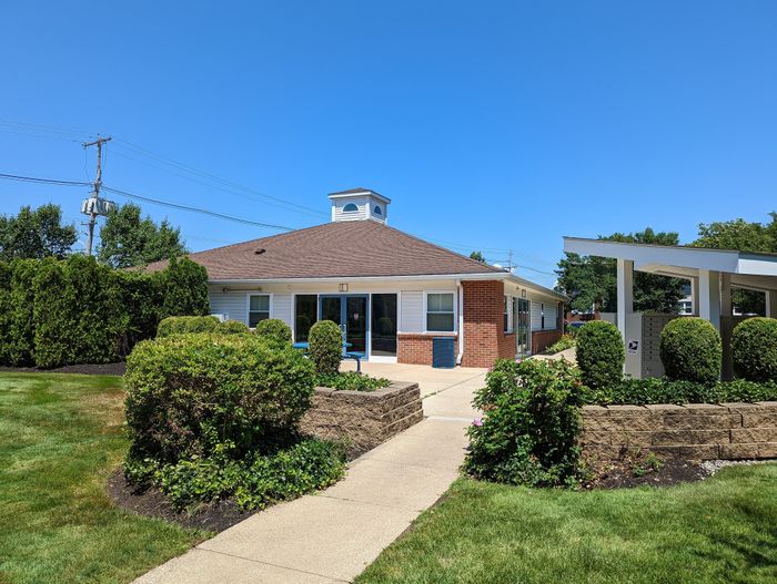 Charming building exterior with a well-maintained lawn, vibrant green shrubs, and clear blue skies highlighting the inviting atmosphere.