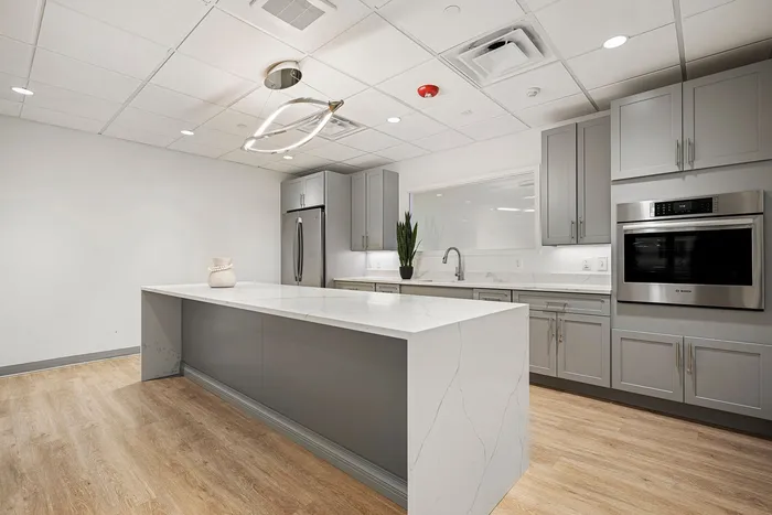 Elegant modern kitchen featuring sleek grey cabinetry, stainless steel appliances, and a spacious white marble island with stylish lighting.