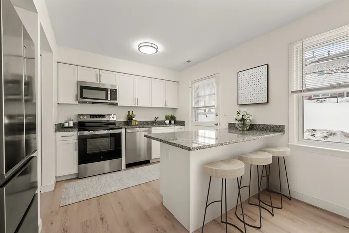 Modern kitchen with granite countertops, sleek stainless steel appliances, and elegant bar seating under natural light.