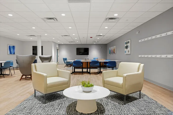Bright and contemporary shared space featuring plush seating, modern decor, and a versatile meeting area with stylish blue chairs.