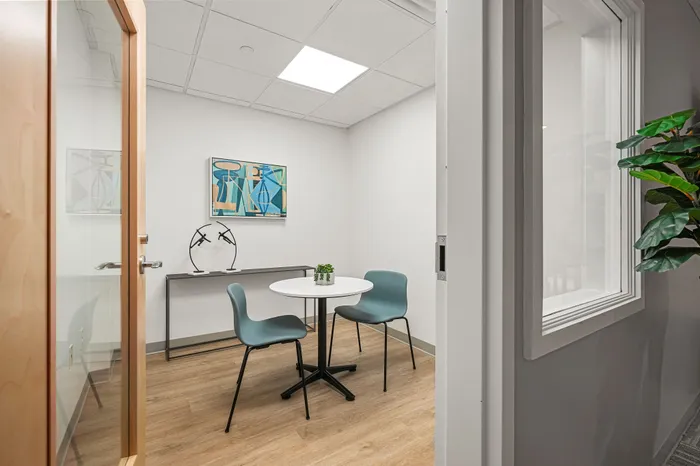 Modern small office space with a round table, stylish blue chairs, vibrant artwork, and natural wood flooring.
