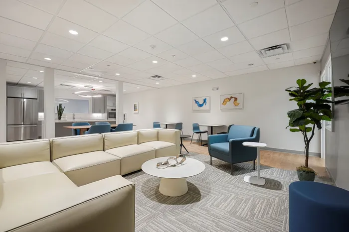 Contemporary living area with elegant beige sectional, modern blue chairs, a stylish round coffee table, and a sleek kitchen in the background.