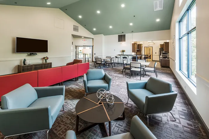 Modern communal living space featuring stylish seating, vibrant red couches, and a well-lit dining area, perfect for social gatherings.