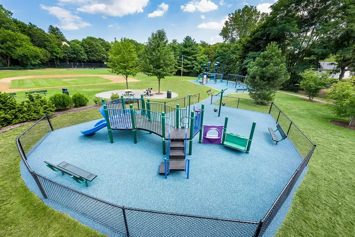 Inviting playground with vibrant equipment surrounded by lush greenery and adjacent to a baseball field, perfect for family fun.