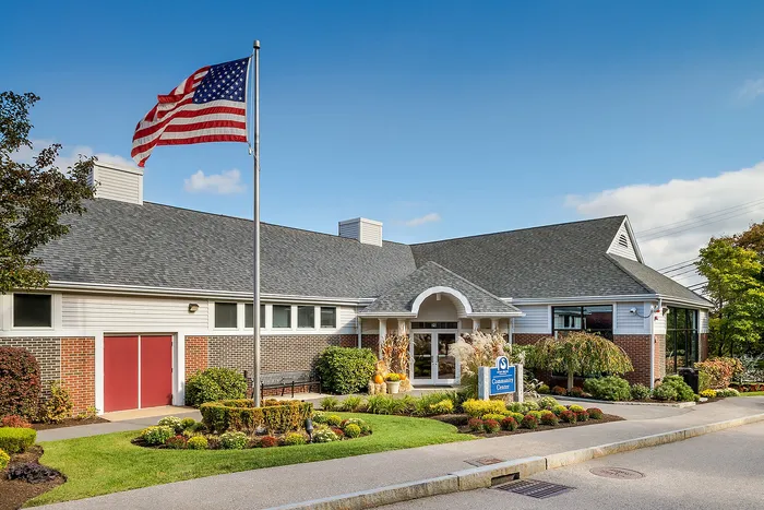 Inviting community center with lush landscaping, striking architecture, and a prominently flying American flag under a clear blue sky.