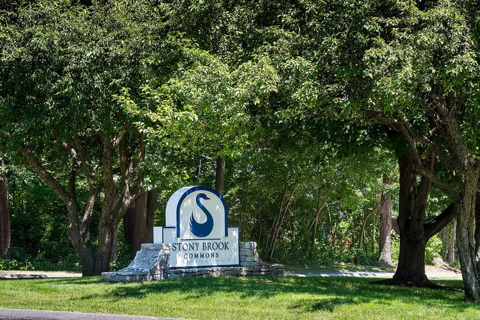 Inviting entrance of Stony Brook Commons adorned with lush green trees and a charming stone sign under the summer sun.