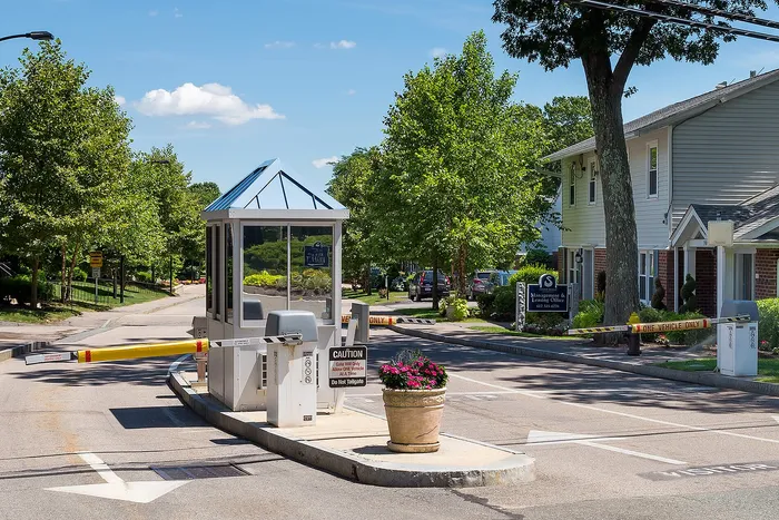 Inviting entrance to a gated apartment community with lush greenery, trees, and a welcoming guard booth.