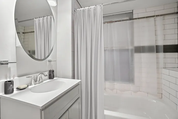 Elegant bathroom with a sleek white vanity, stylish sink, and modern circular mirror, exuding a spa-like ambiance.
