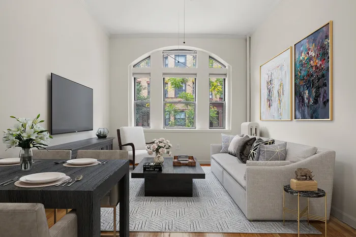Elegant living room with modern decor, featuring a plush gray sofa, sleek black dining table, and large arched windows offering a charming outdoor view.