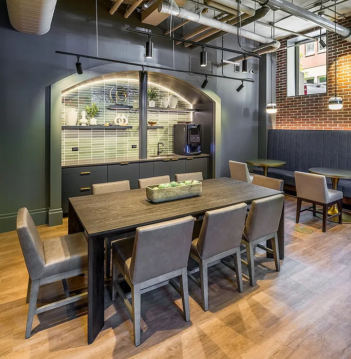 Modern dining area with sleek wooden table, comfortable seating, and stylish kitchenette set against exposed brick walls.