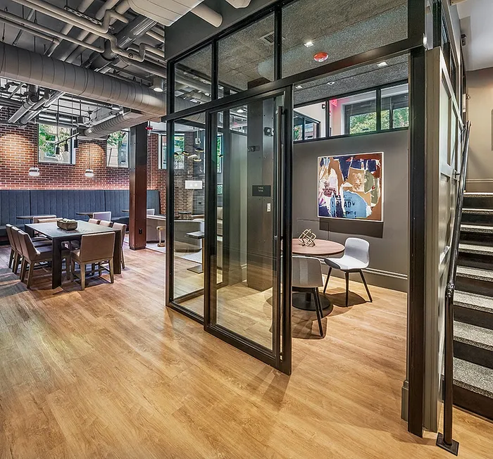 Modern industrial-style room with exposed brick walls, stylish wood flooring, and glass meeting enclosure, ideal for dynamic living and workspaces.