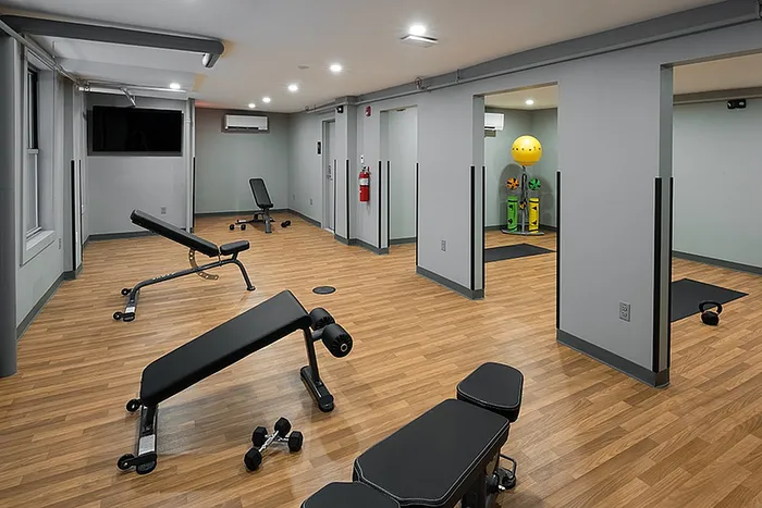 Modern fitness room with wooden flooring, workout benches, free weights, and ample open space for exercise routines.