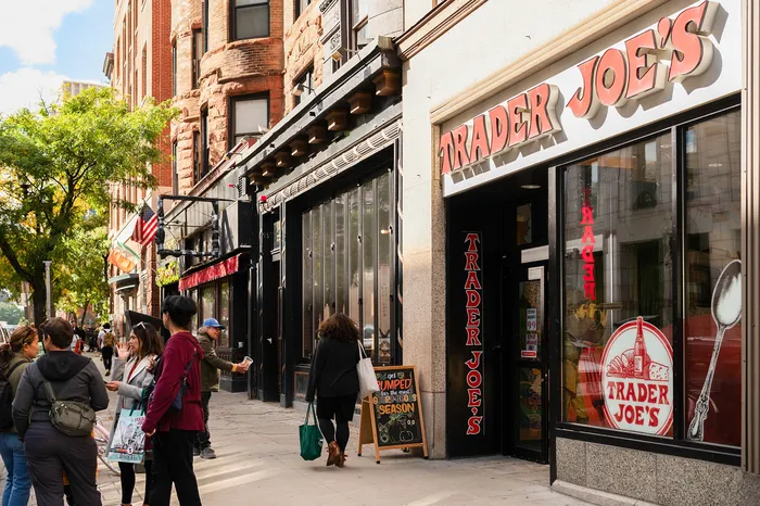 Vibrant street scene with people enjoying a sunny day outside Trader Joe's, showcasing lively urban atmosphere and historic brick architecture.