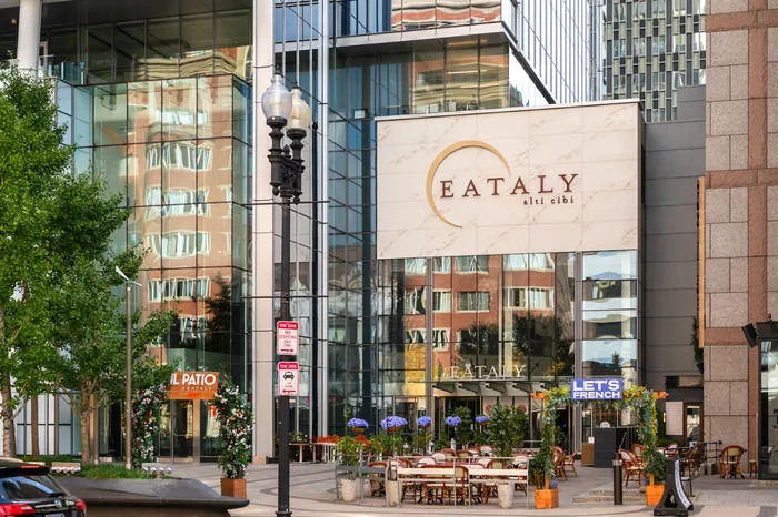 Vibrant cityscape with a modern glass building showcasing an inviting outdoor dining area adorned with colorful flowers and chic seating.