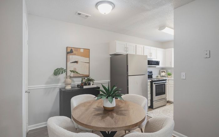 Charming dining area with a round wooden table, stylish modern chairs, and adjacent sleek kitchen featuring stainless steel appliances and crisp white cabinetry.