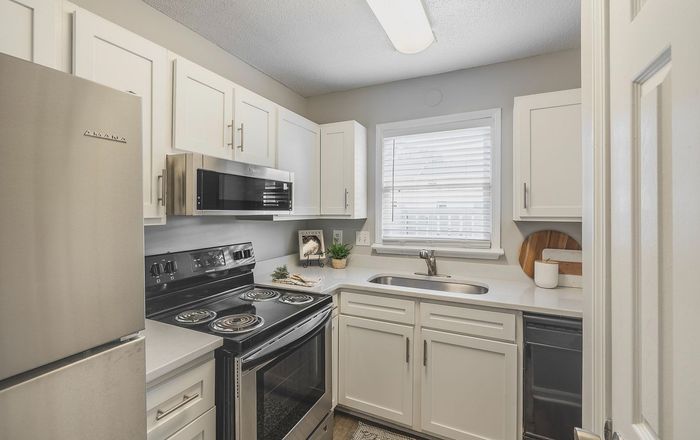 Bright and modern kitchen with stainless steel appliances, white cabinetry, and natural light from a window. Perfect for culinary creativity.