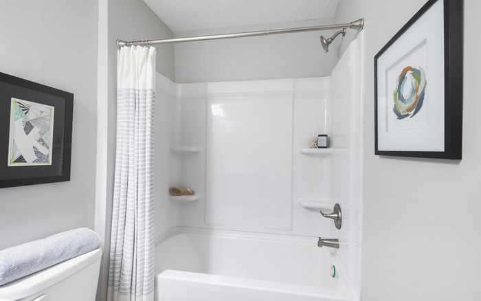 Bright and modern bathroom featuring a sleek bathtub with stylish gray-and-white shower curtain and contemporary wall art.