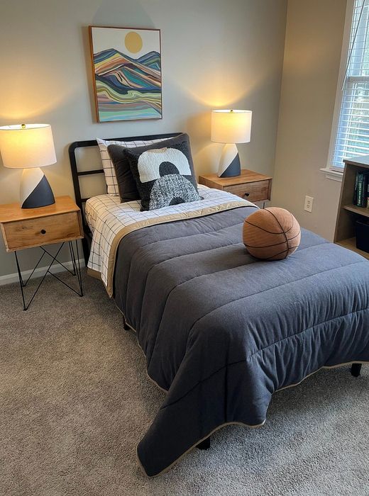 Cozy bedroom with modern decor featuring a twin bed with gray bedding, stylish lamps, and a vibrant abstract painting, exuding warmth and comfort.