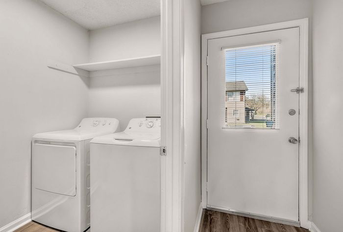 Bright laundry room with modern washer and dryer, featuring a door with a window view of outdoor scenery, perfect for convenient living.
