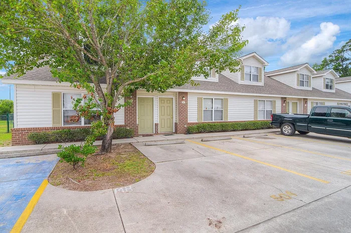 Charming townhome exterior with light brick accents, green doors, and ample parking under a clear blue sky.