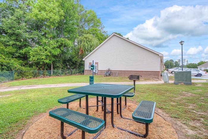 Charming outdoor space featuring a picnic table and barbecue grill, surrounded by lush greenery and a cozy residential setting.