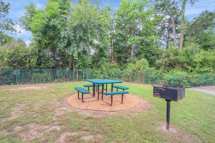 Inviting outdoor picnic area with a green table set and barbecue grill, surrounded by lush greenery for a perfect leisure retreat.