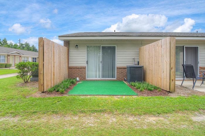 Charming patio area with sliding glass door, enclosed by wooden fencing, and lush greenery for privacy and tranquility.