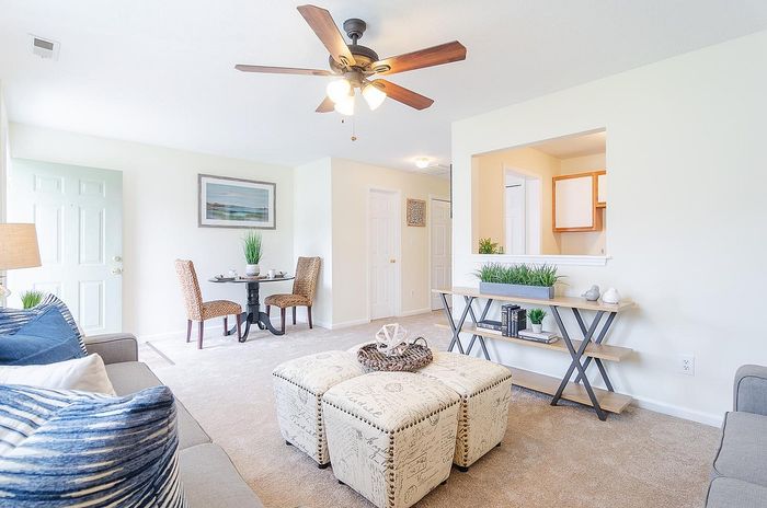 Bright and inviting living room with plush seating, stylish ottomans, and modern decor, featuring a cozy dining nook and ceiling fan.
