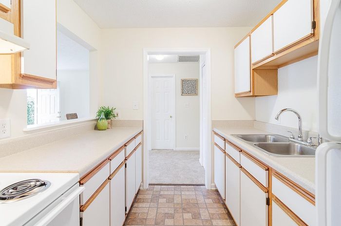 Bright and inviting kitchen with sleek countertops, stainless steel sink, and ample storage, leading to a cozy carpeted dining area.