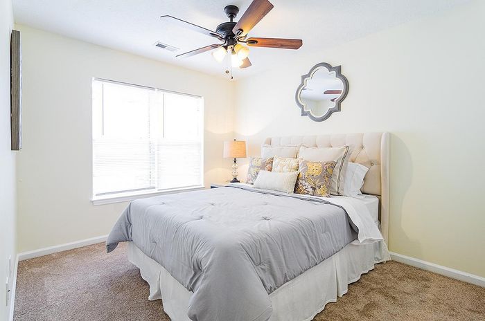 Inviting bedroom with a plush queen-sized bed, elegant tufted headboard, and a stylish ceiling fan, bathed in natural light from a large window.