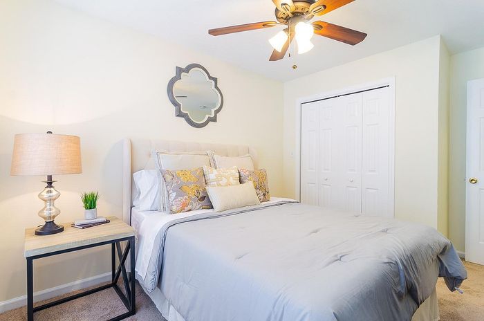 Inviting bedroom with plush bedding, decorative pillows, stylish mirror, and a warm ambiance under elegant ceiling fan lighting.