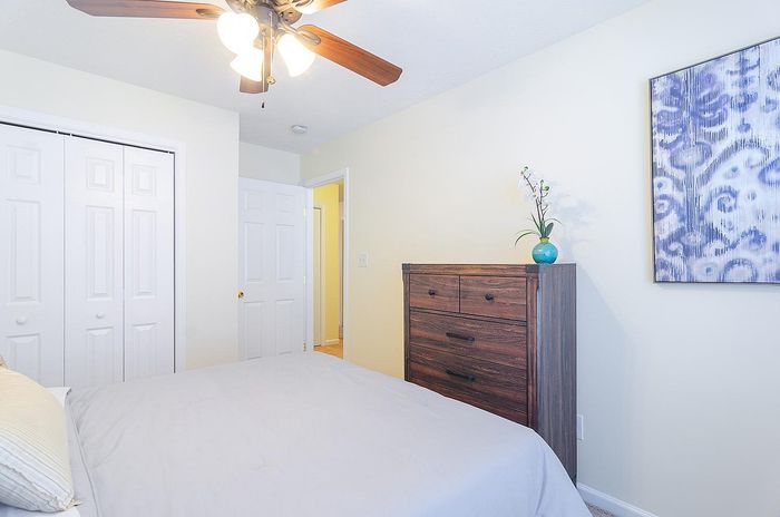 Bright bedroom with modern ceiling fan, elegant wooden dresser, and floral wall art creating a cozy atmosphere.