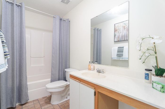 Modern bathroom featuring sleek white fixtures, a spacious countertop, and elegant decor including a floral arrangement and subtle artwork.