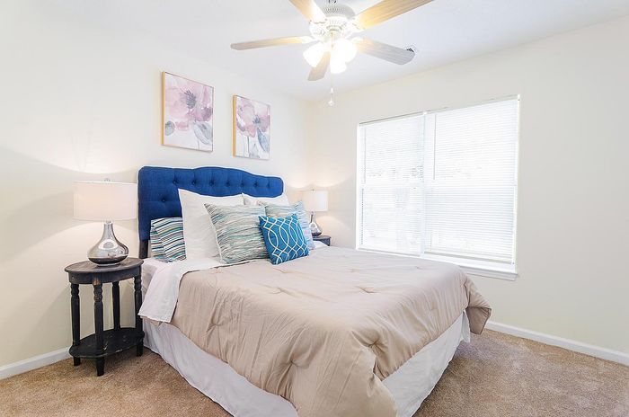 Bright and inviting bedroom with plush bedding and elegant decor, featuring a cozy blue headboard and stylish ceiling fan.
