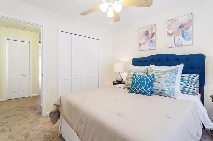 Inviting bedroom featuring a plush blue headboard, cozy bedding with vibrant cushions, decorative wall art, and ample closet space, perfect for a restful retreat.