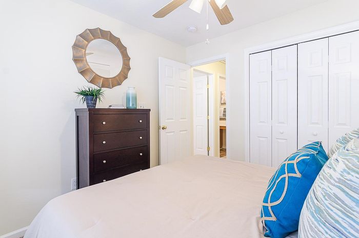 Inviting bedroom with elegant wooden dresser, stylish mirror, and vibrant blue pillows, offering a serene and cozy atmosphere.