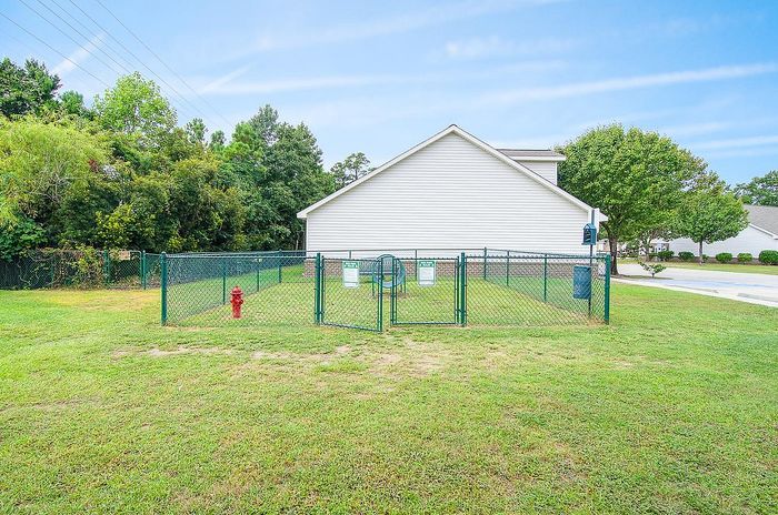 Inviting fenced pet area beside a charming white house, surrounded by lush greenery and blue skies.