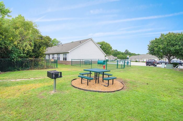 Inviting outdoor picnic area with modern seating and a barbecue grill, set against a backdrop of charming residential homes and lush greenery.