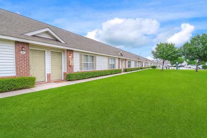 Charming row of single-story apartments with manicured lawns and inviting front entrances under a clear blue sky.