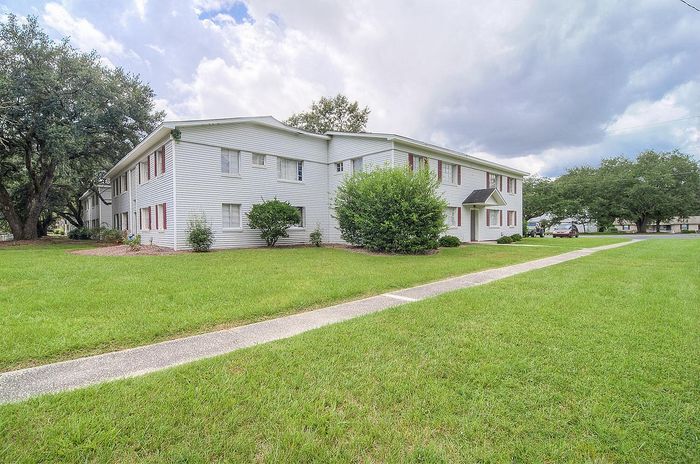 Charming white apartment complex surrounded by lush greenery and a spacious lawn, perfect for serene living.