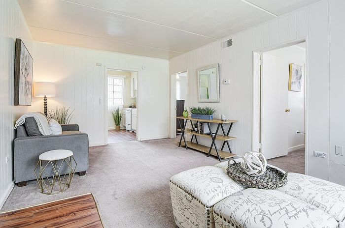 Bright and inviting living area with modern decor, cozy armchair, and a view into a well-appointed kitchen.